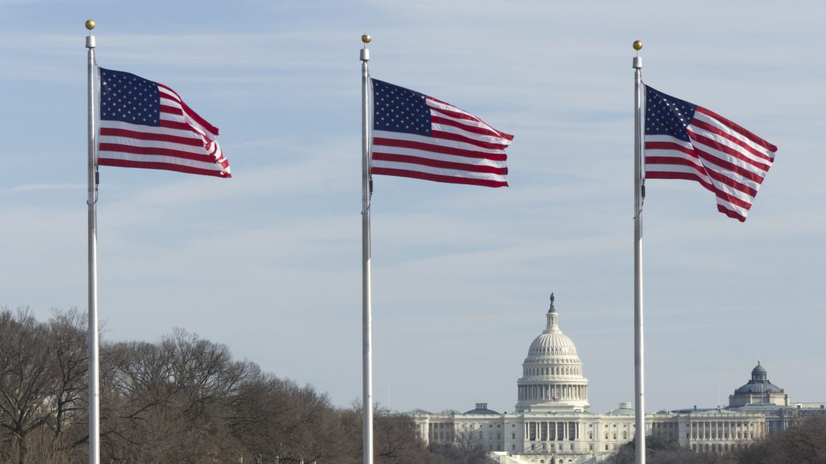 Tres banderas de los Estados Unidos a todo lo alto con el edificio del Capitolio de los Estados Unidos en la parte inferior derecha