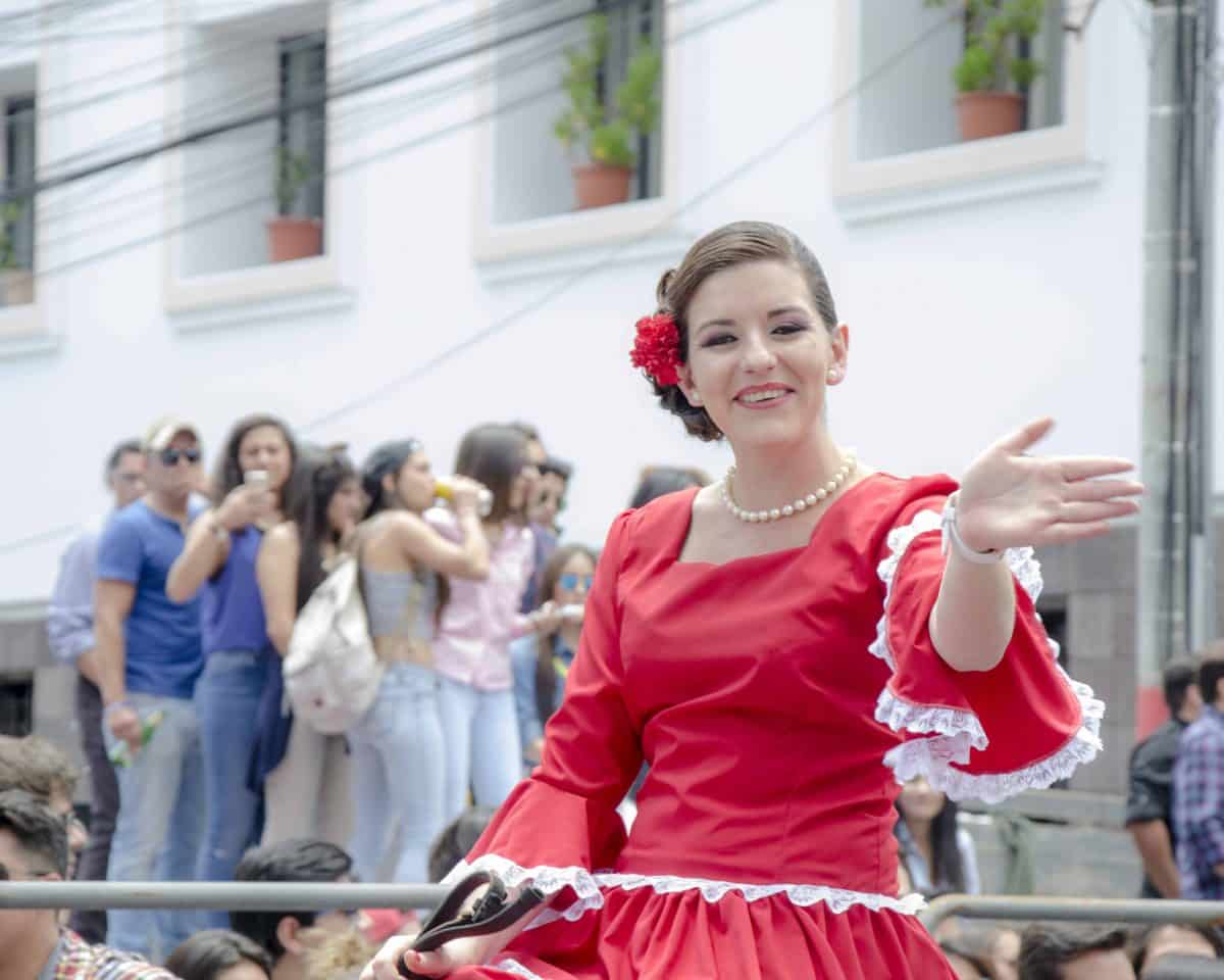 A woman dressed in red colonial-style dress waves to the crowd.
