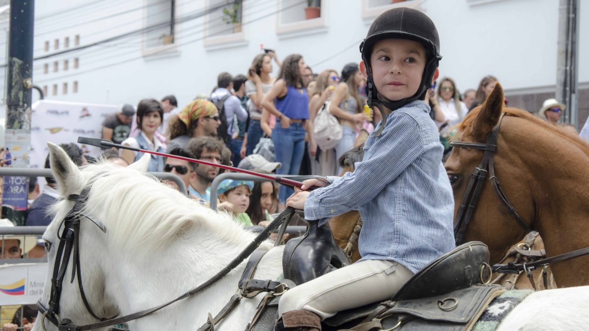 A child in riding helmet and clothes looks back over her shoulder