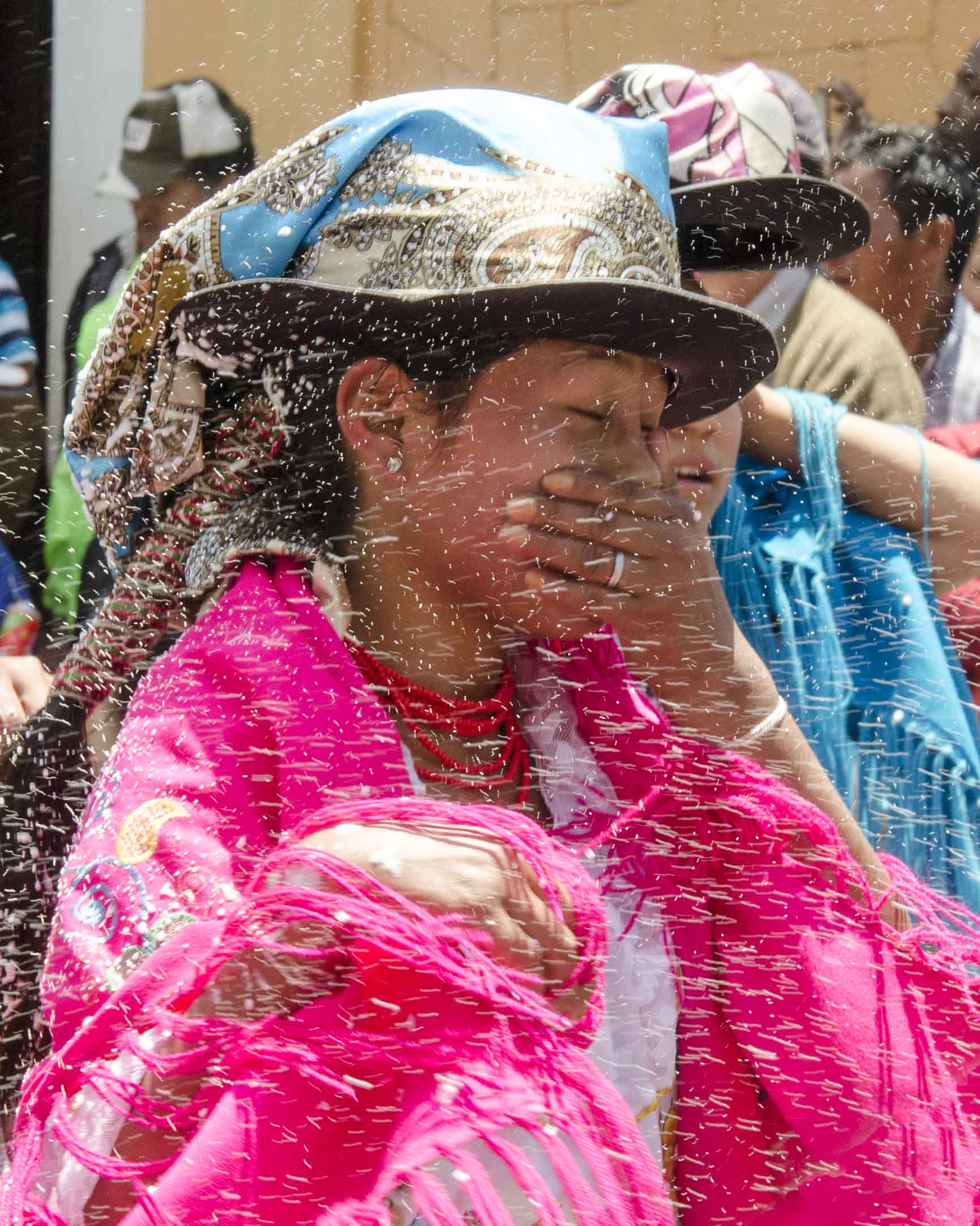 Una bailarina se cubre la cara para evitar que le entren carioca, o espuma de fiesta, en la boca; Guaranda, Ecuador | ©Angela Drake Carnaval en Guaranda, Ecuador