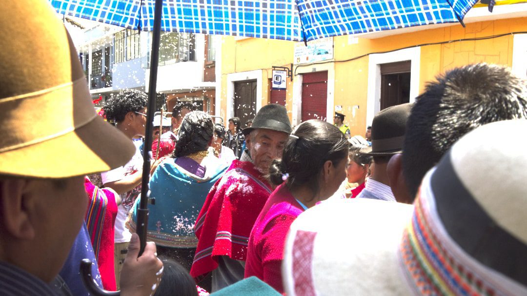 La sombra ayuda en un día caluroso, carnaval en Guaranda, Ecuador | ©Angela Drake Personas de pie a la sombra de un paraguas