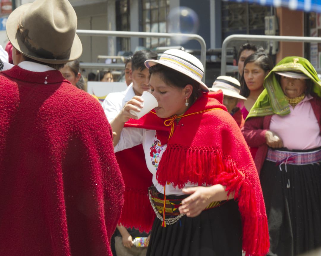 El refrigerio fue importante en este día caluroso, Guaranda, Ecuador | ©Ángela Drake Mujer de rojo, chal de lana bebiendo de un vaso de papel
