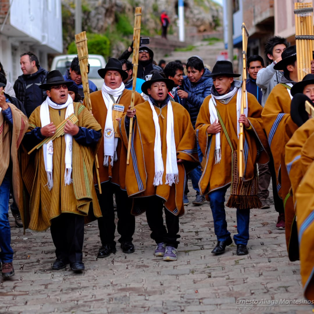 Cantantes vestidos en ponchos de amarillo oscuro bajan a un calle para empezar las festividades