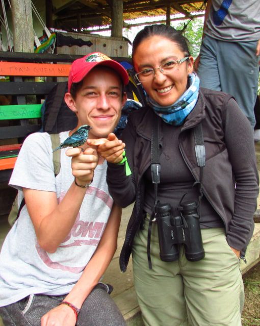 Fernanda Salazar con un estudiante Un pequeño pájaro está encaramado en el dedo de un estudiante de pie junto a su maestro.