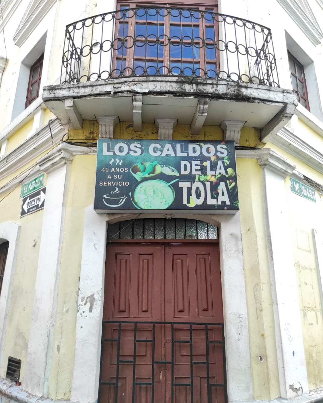 A sign above a wooden door says "Los Caldos de La Tola"
