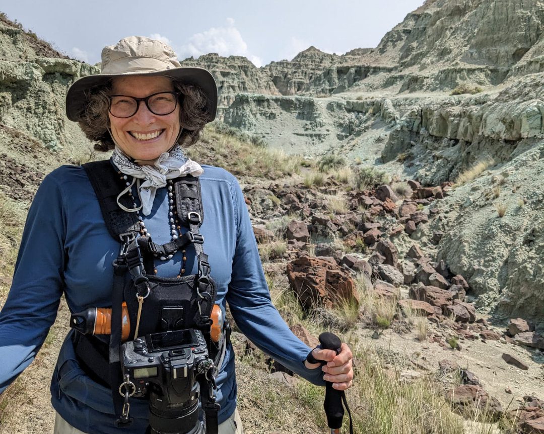 Angie con sus bastones de senderismo en el Monumento Nacional John Day Fossil Beds de Oregón | ©Ernest Scott Drake Mujer con cámara y equipo de senderismo posa para la cámara con una enorme sonrisa en la cara