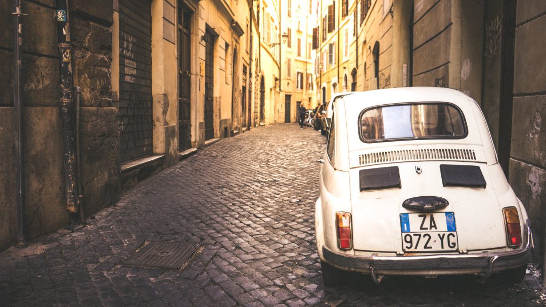 Coche blanco de época aparcado en calles adoquinadas.