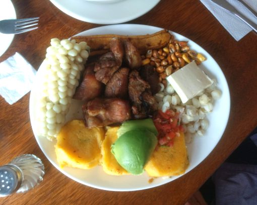 Un plato completo de fritada que incluye cerdo frito, hamburguesas de patata, mazorca de maíz, maíz tostado, maíz, queso y aguacate.