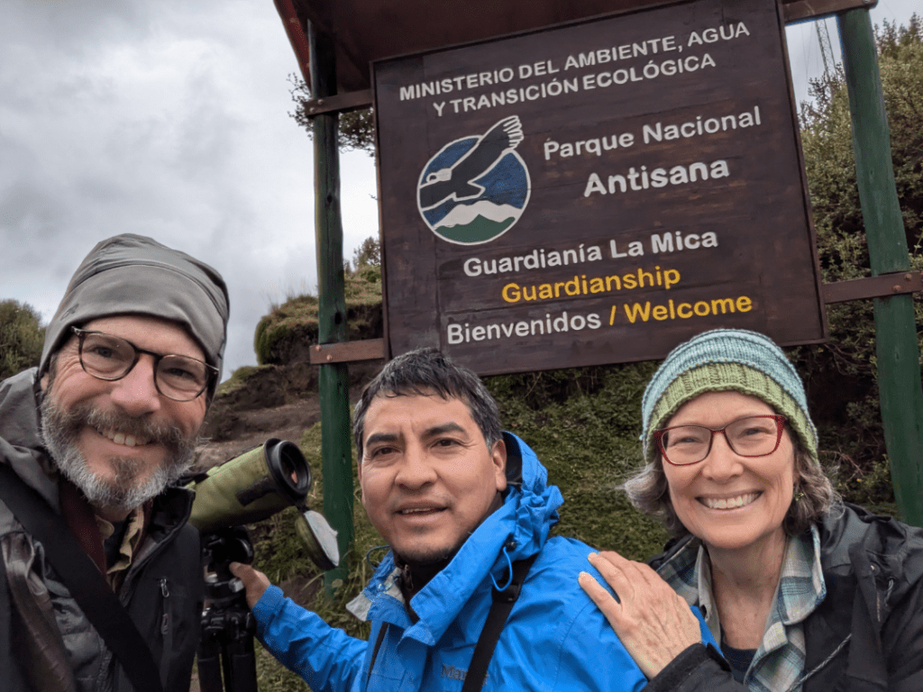 Tres personas de pie frente a un cartel del Parque Nacional Antisana