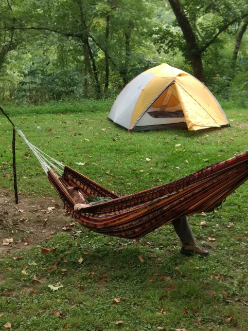 Un hombre en una hamaca con una tienda REI para 4 personas al fondo.