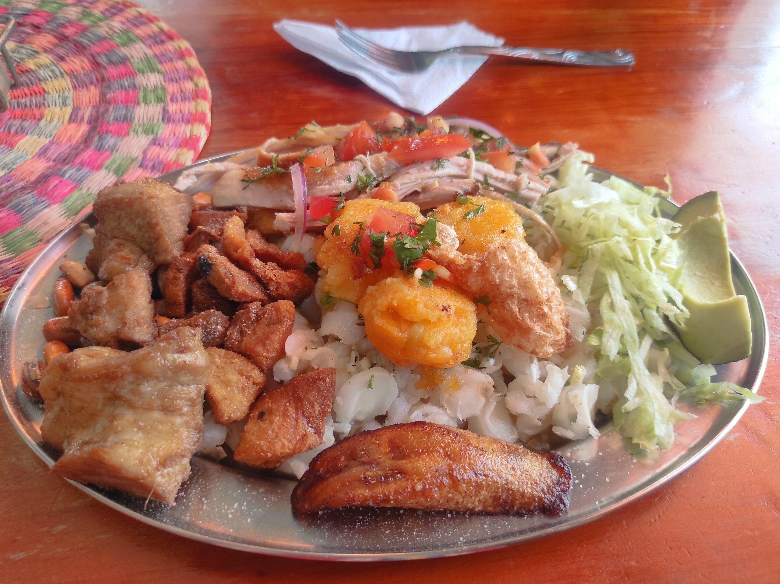 Hornado pastuso - Ecuador A plate of Ecuadorian-style Hornado Pastuso, roasted pork with fixings like mote, sweet plantain, and potato pancakes.